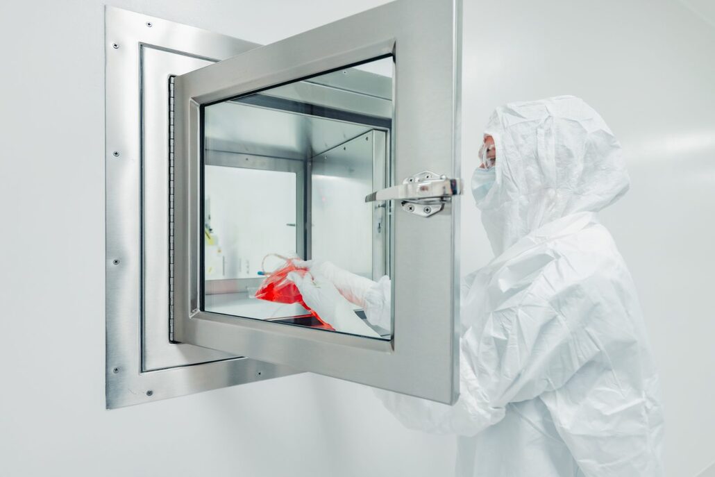 Gowned operator passing materials through a cleanroom pass-through window