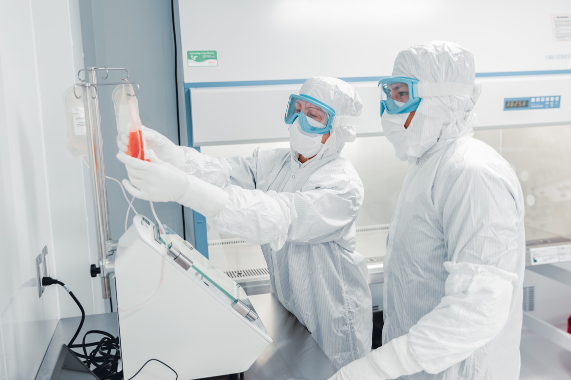 Two operators in full cleanroom gowns and goggles working at a cell processing system