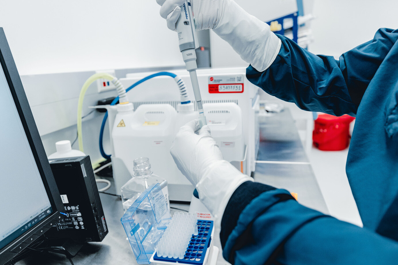 Gloved hands pipetting samples into a tube rack at a lab bench